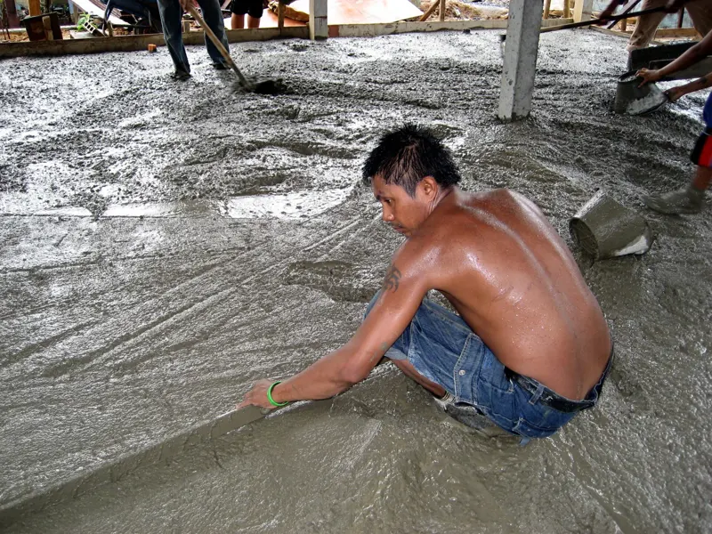Worker spreading fresh concrete across a new house slab